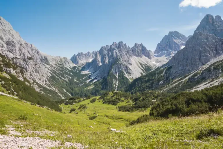 Albanian Alps 1 Dramatic, jagged grey limestone peaks of the Accursed Mountains rise steeply, surrounding a pristine, deep green valley with a small village and church, Albanian Alps, Albania.