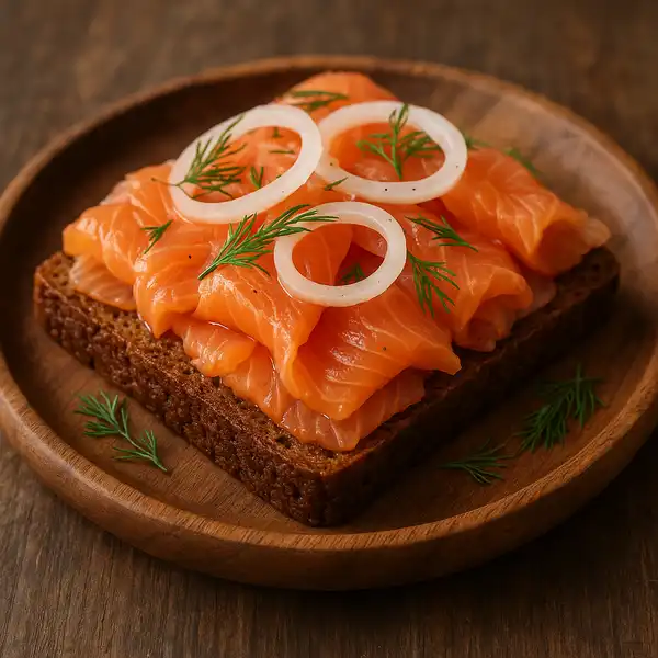 A thick slice of smoked salmon rests on a slice of dark rye bread, topped with thinly sliced red onions and fresh dill