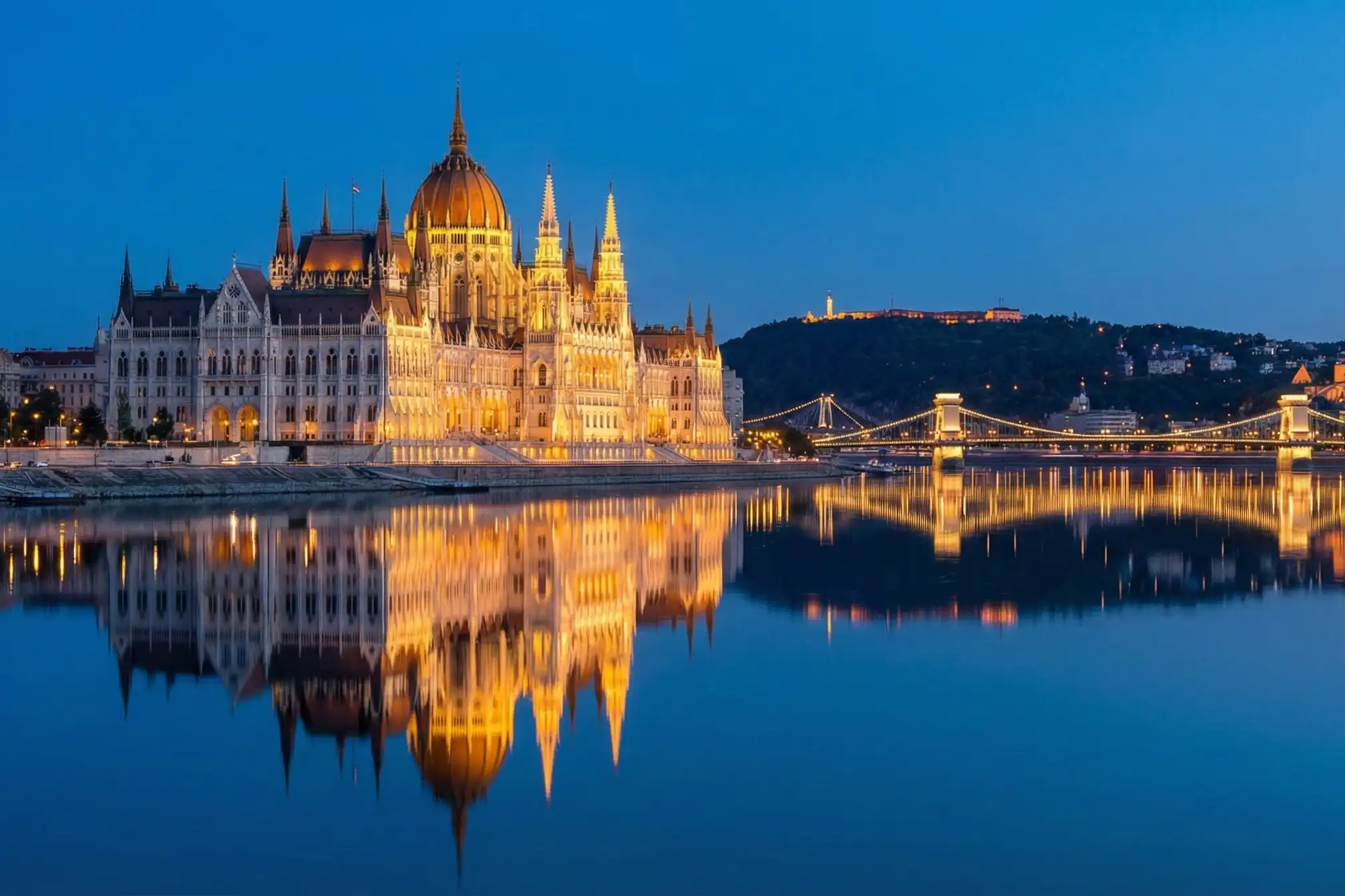 Illuminated Hungarian Parliament Building and Chain Bridge in Budapest at twilight reflecting on the Danube River.