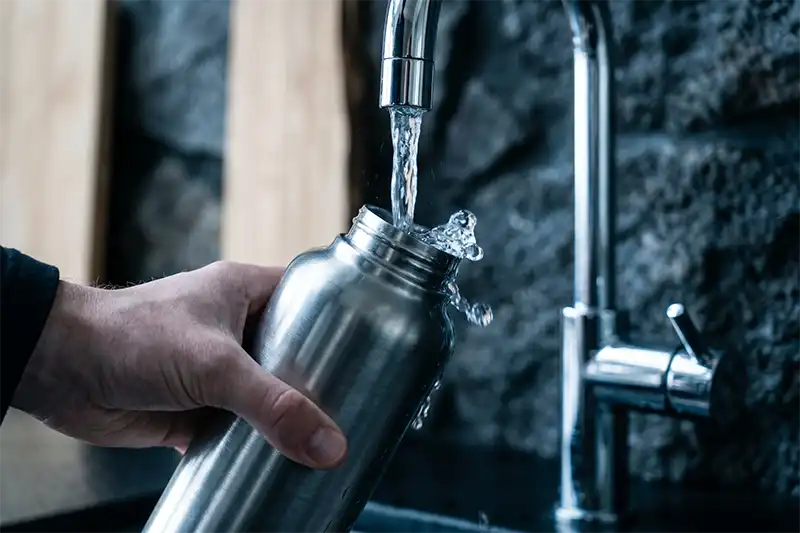 Skip the Bottled Water "Tourist Tax" 1 Close-up of a reusable metal bottle being filled with fresh Icelandic tap water in a modern setting.