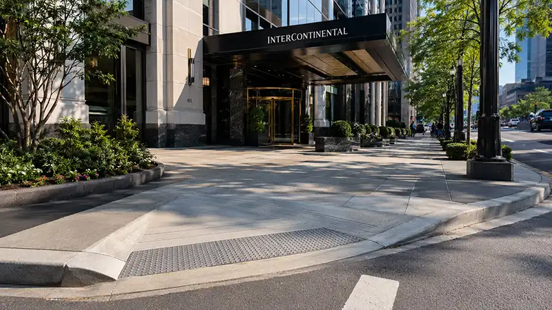 Travel Tips 11 A smooth city sidewalk featuring a gentle curb ramp that leads toward the elegant entrance of a premium hotel.