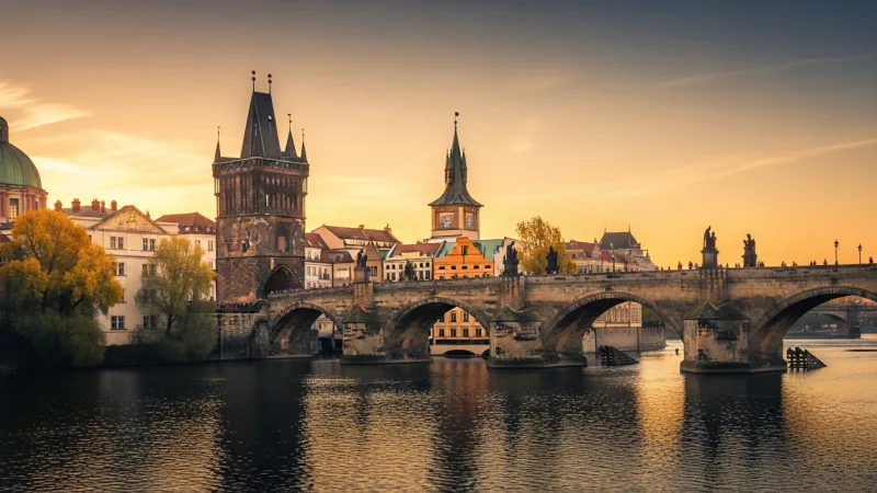 Golden Hour Ascent 6 The Old Town Bridge Tower bathed in the warm light of sunrise or sunset, with the Charles Bridge stretching out, and the Vltava River reflecting the sky.