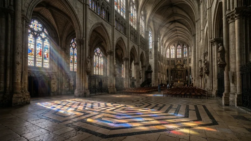Walk the Basilica's Historic Labyrinth 3 Interior of Saint-Quentin Basilica showing sunbeams illuminating an ancient stone labyrinth on the nave floor.